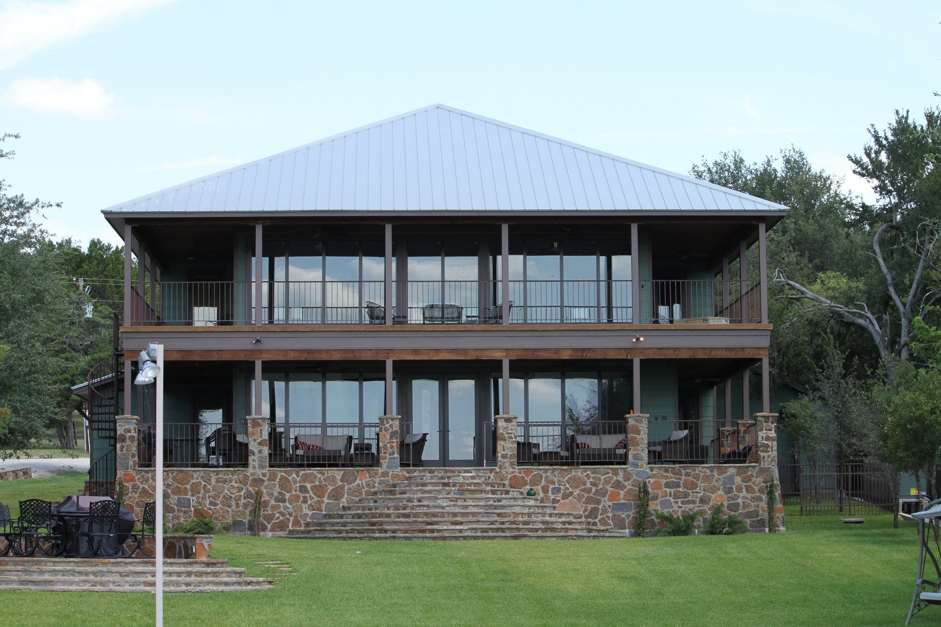 Two-story custom home with wraparound porches, metal roof, and stone foundation built by Tincher's Custom Homes in Palo Pinto County, TX