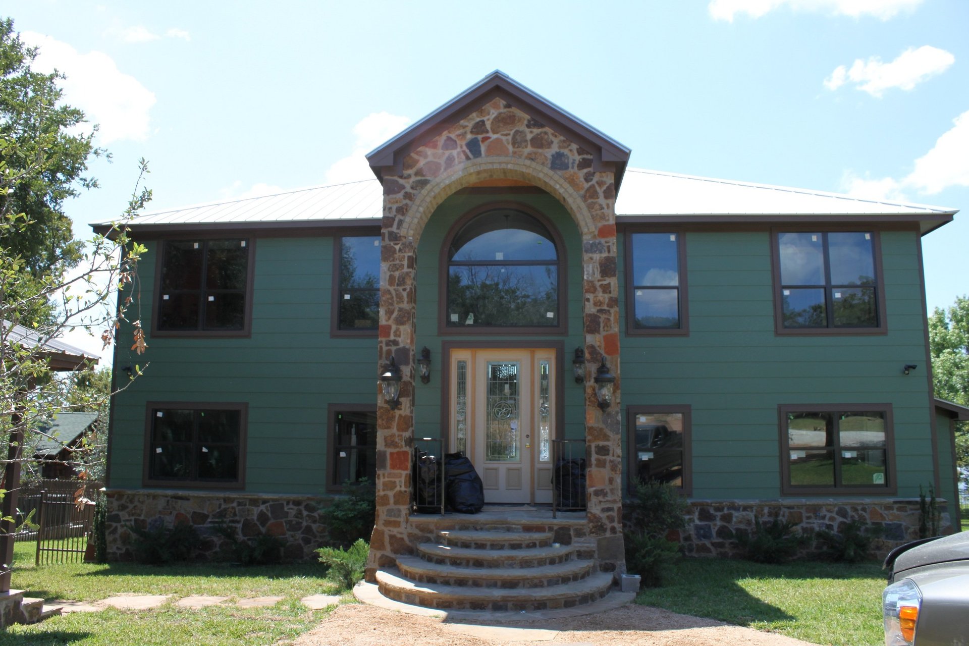 Stone arch entry with board-and-batten siding and metal roof — Tincher's Custom Homes