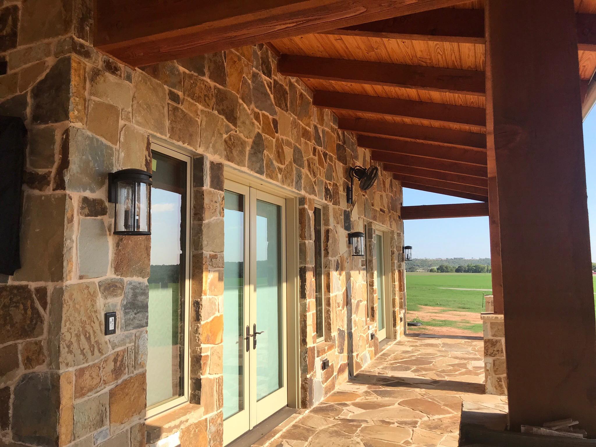 Covered timber frame entry porch with ornate wrought-iron double doors and native fieldstone walls — Tincher's Custom Homes