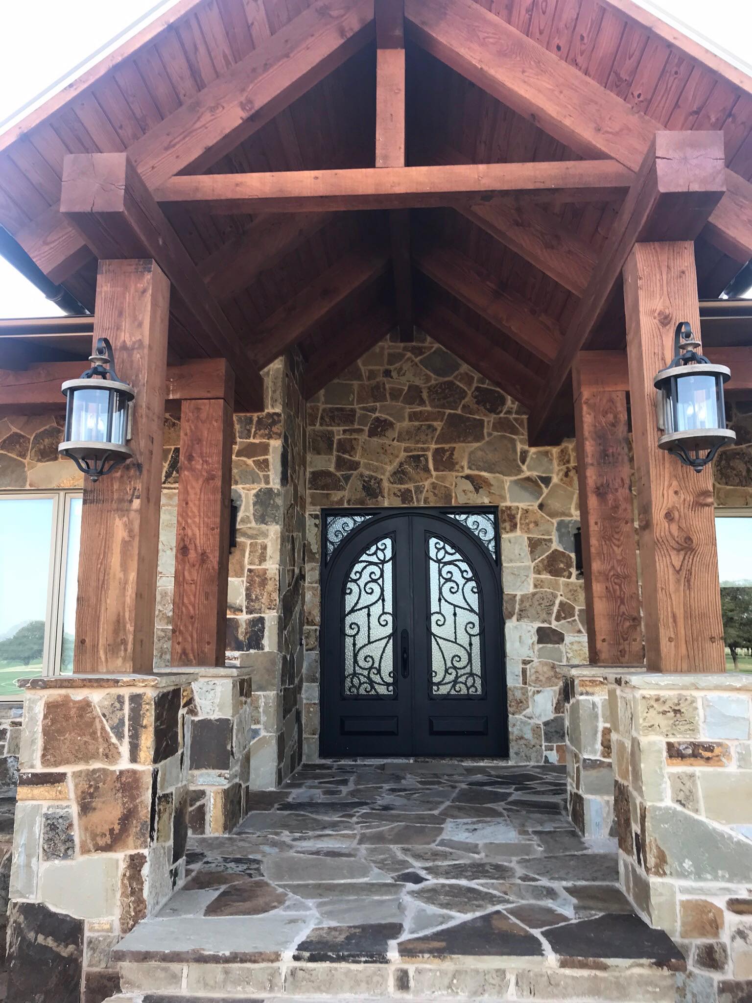 Ornate wrought-iron arched double entry doors set in native fieldstone — custom detail work by Tincher's Custom Homes