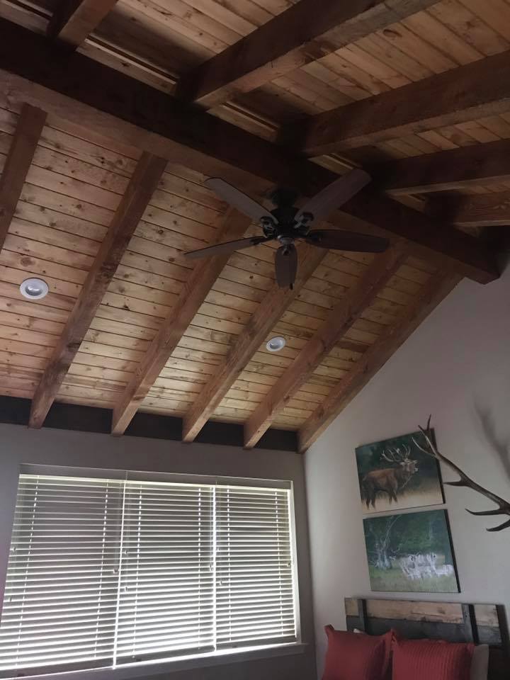 Barndominium interior with vaulted cedar tongue-and-groove ceiling, exposed timber beams, ceiling fan, and wildlife art — Tincher's Custom Homes