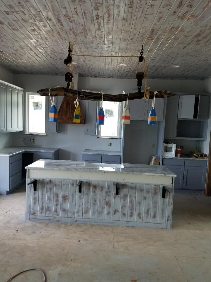 Coastal-style custom kitchen with driftwood pendant light, lobster buoy accents, distressed island, and gray-blue shaker cabinets — Tincher's Custom Homes